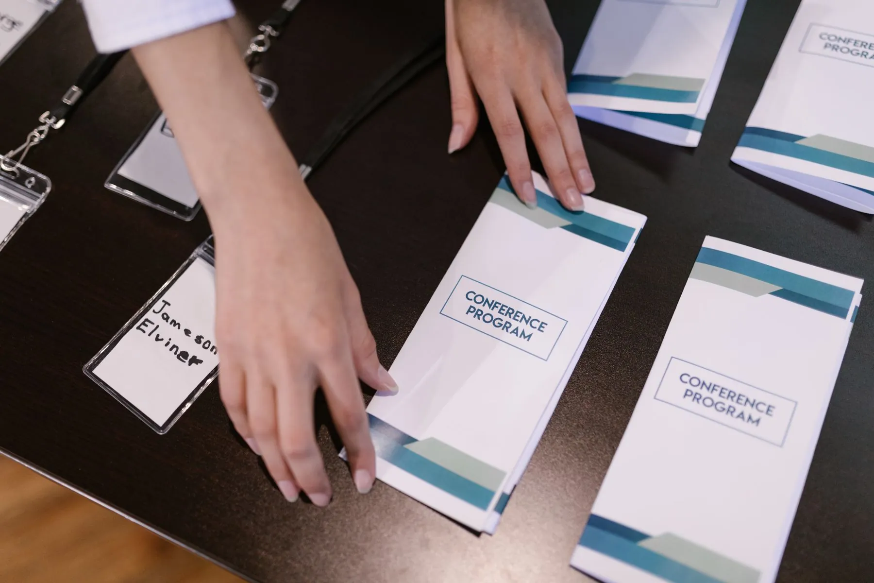 Hands arranging conference programs and name badges at a registration table